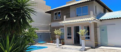 A two-story house with a swimming pool, potted plants, and a clear blue sky.
