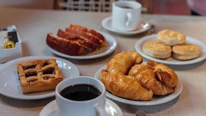 Een ontbijttafel met croissants, koekjes, een taart en koffiekopjes.
