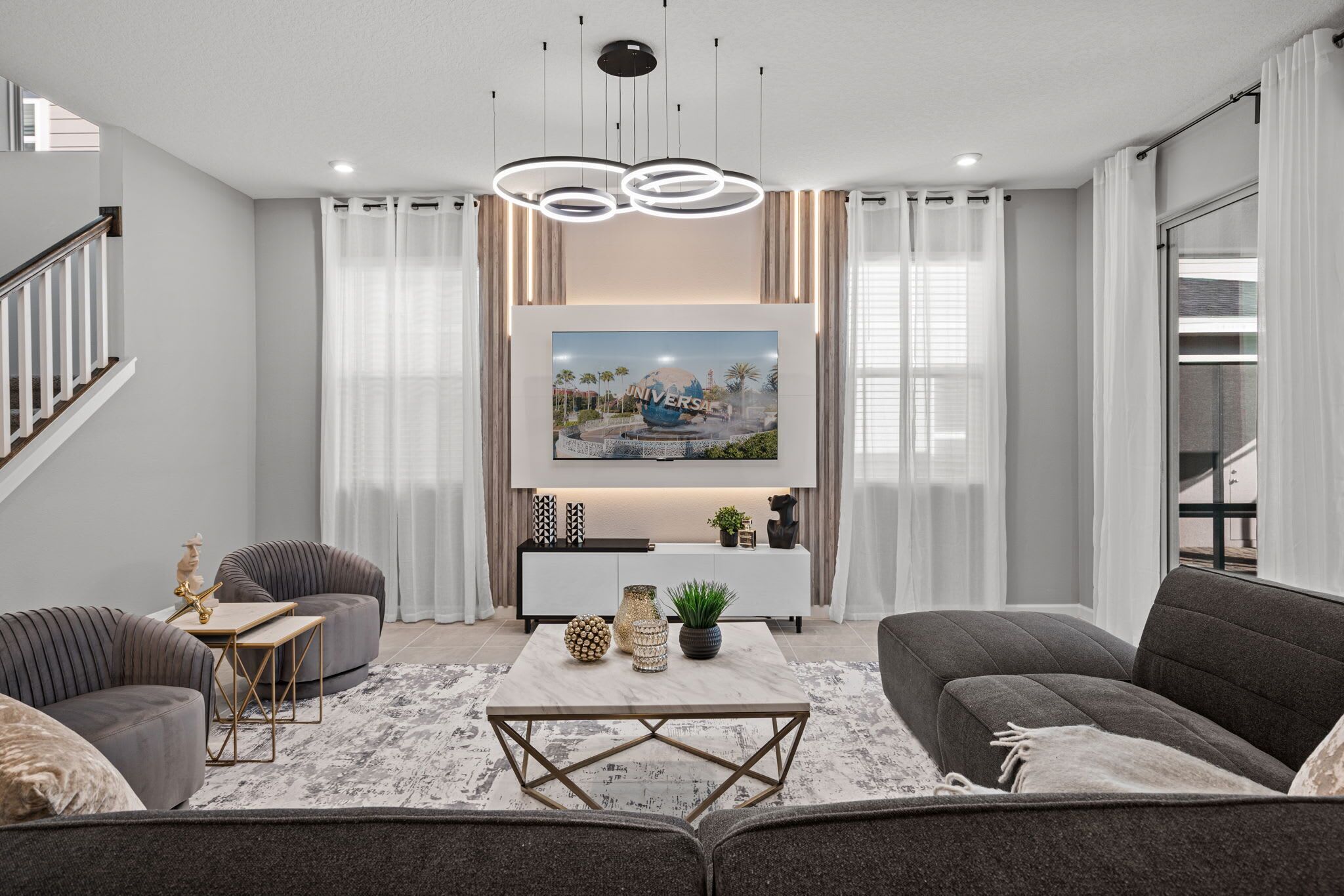 A modern living room with a flat-screen TV mounted above a white console table, grey sofas, and a coffee table with decorative items.