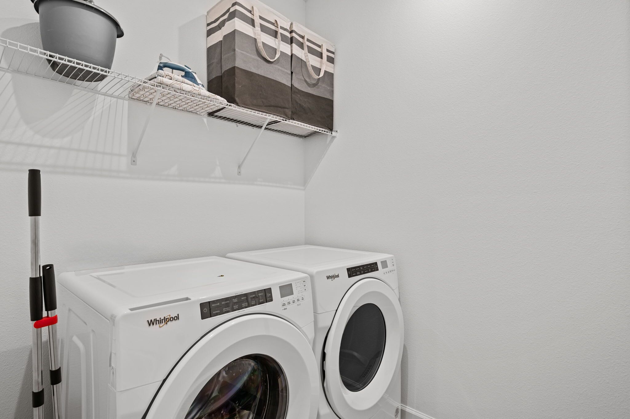 Une buanderie équipée de deux machines à laver Whirlpool, d’un étendoir métallique et d’un meuble de rangement.