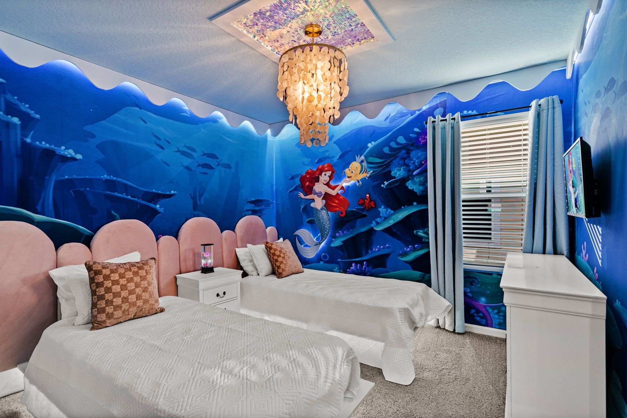 A bedroom with two beds, a chandelier, and a mural of an underwater scene.