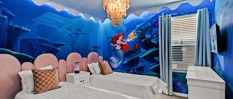 A bedroom with two beds, a chandelier, and a mural of an underwater scene.