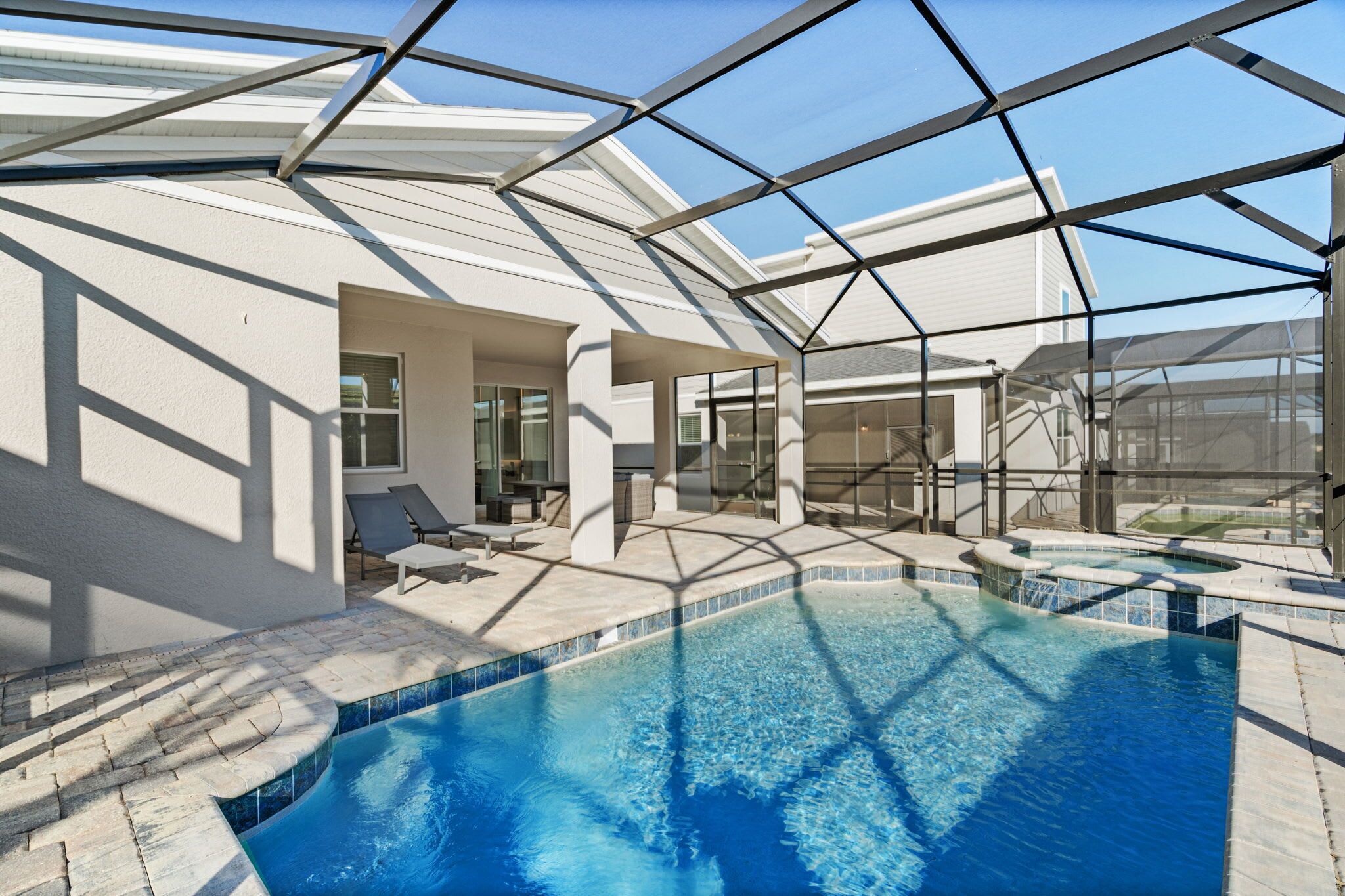 A modern indoor swimming pool with a glass ceiling, lounge chairs, and a patio area.