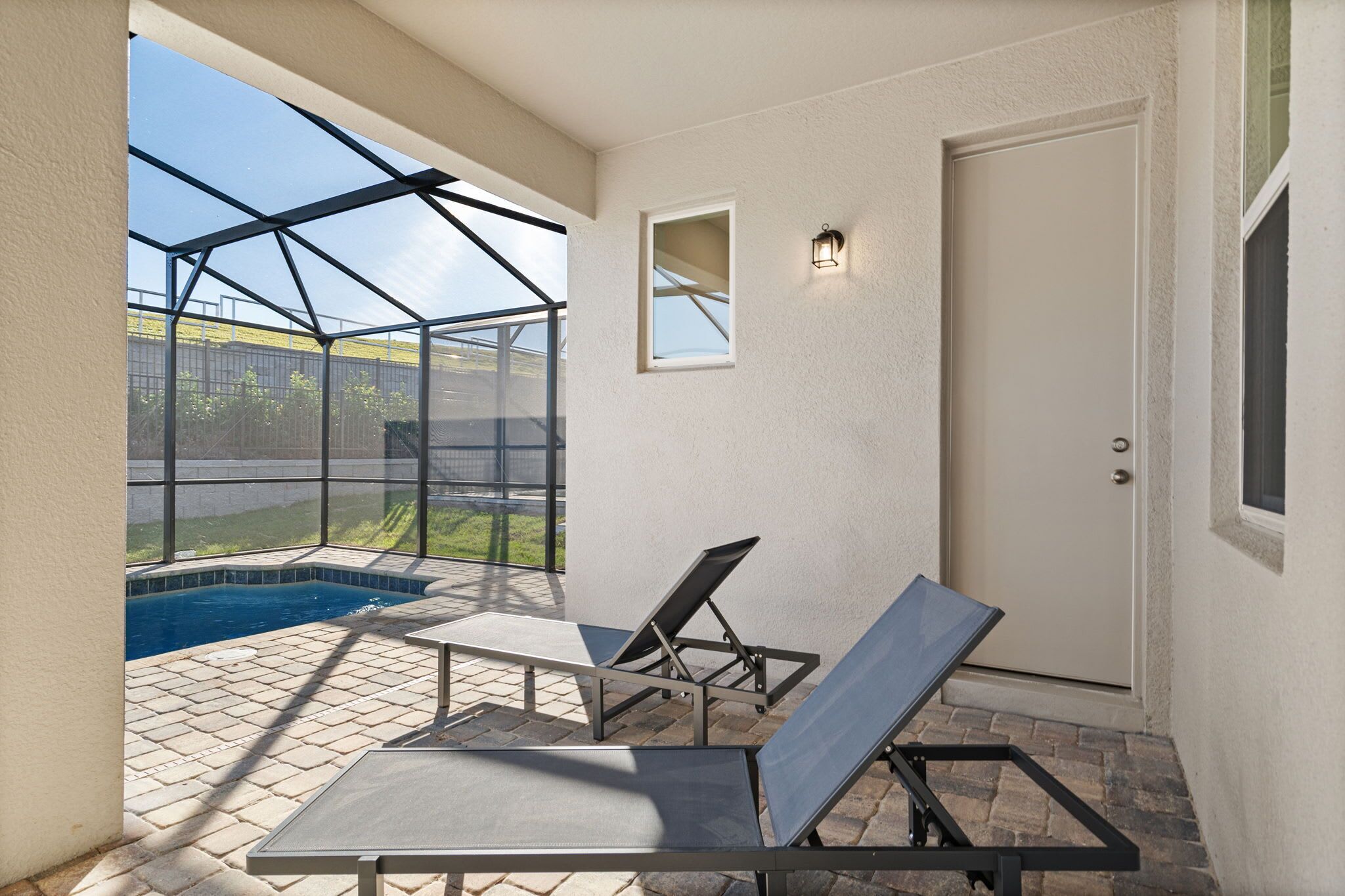 Überdachte Terrasse mit Swimmingpool, zwei Liegestühlen und einer Tür.