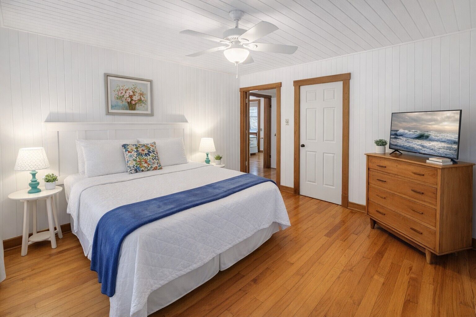 A bedroom with a bed, a dresser, a television, and a ceiling fan.