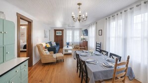 Un coin repas avec une table en bois dressée pour quatre personnes, flanquée de deux chaises. Un canapé et une petite table avec une lampe se trouvent à l’arrière-plan.