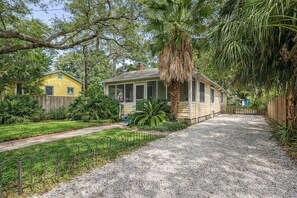A single-story house with a covered porch, surrounded by a gravel driveway and lush greenery. - Tybee Island Sunrise (Tybee Island)