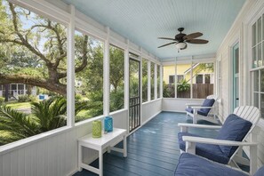 A covered porch with white chairs and a table, large windows, and a ceiling fan. - Tybee Island Sunrise (Tybee Island)