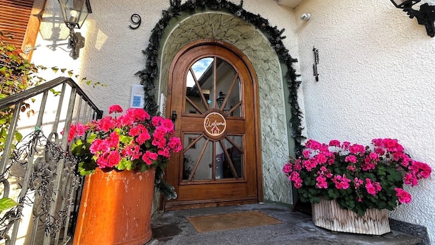 Una puerta de madera con un ventanal circular y un letrero de bienvenida, flanqueada por dos macetas grandes.