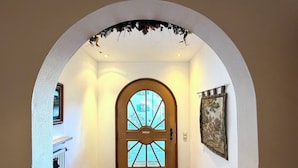 Un pasillo con puerta de madera, suelo de baldosas, felpudo y un cuadro colgado en la pared.