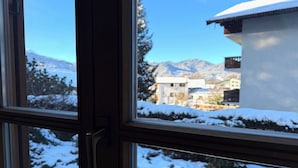 Una ventana con vistas a un paisaje nevado, con árboles cubiertos de nieve y montañas al fondo.