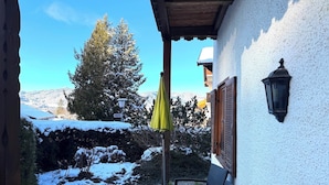 Un patio con mesa y sillas, un paraguas amarillo y vistas a árboles y montañas nevadas.