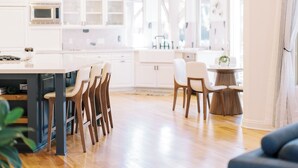 Una cocina moderna con armarios blancos, una isla central y sillas de madera.