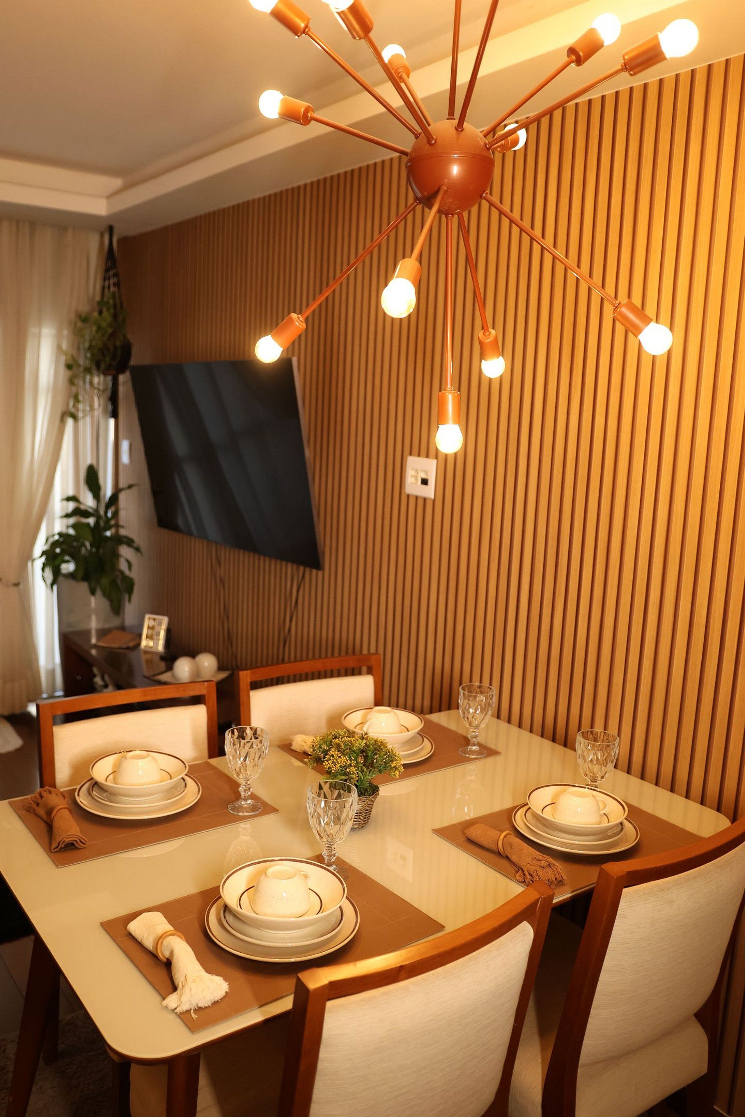 Zona pranzo con lampadario moderno, parete rivestita in legno e tavolo apparecchiato per due.