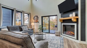 A modern living room with a leather sofa, a fireplace, a dining area with a table and chairs, and a view of the outdoors. - Indoor Pool, Hot Tub & Vols Spirit With Sweeping Mountain Views Smokey's Den by Avantstay (Sevierville)