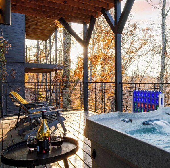A hot tub with a waterfall feature, lounge chairs, and a bottle of wine on a wooden deck with a view of autumn trees. - Indoor Pool, Hot Tub & Vols Spirit With Sweeping Mountain Views Smokey's Den by Avantstay (Sevierville)