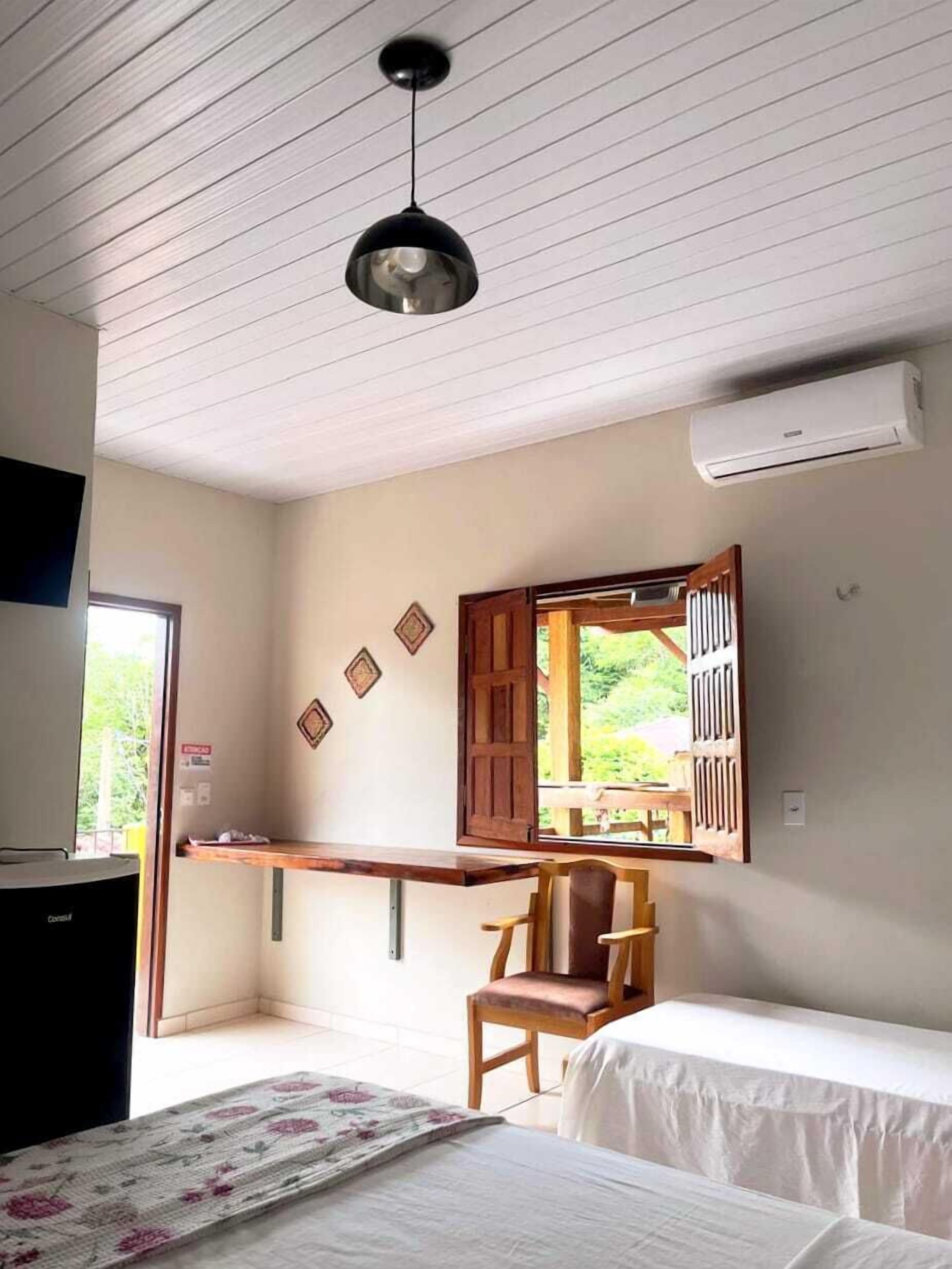 Une pièce avec un lit, une chaise, un bureau et une fenêtre dont les volets sont ouverts.