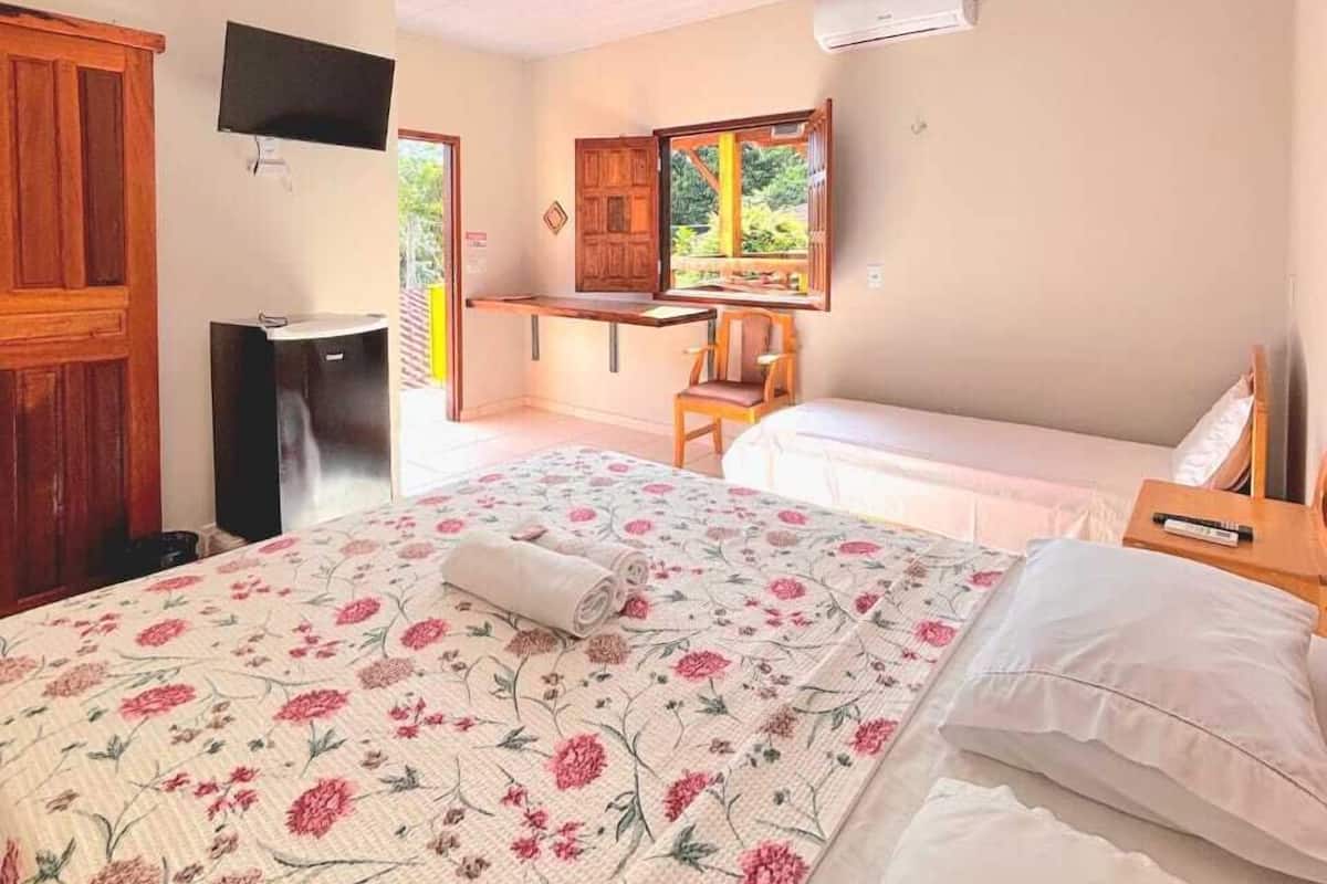 A bedroom with a bed, a desk, a TV, and a window with a view of greenery.