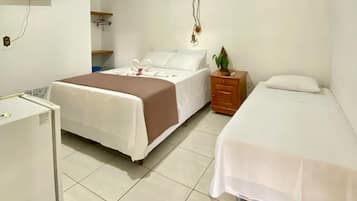 Habitación de hotel con dos camas, un refrigerador pequeño, un televisor montado en la pared y una mesita de noche con una planta.