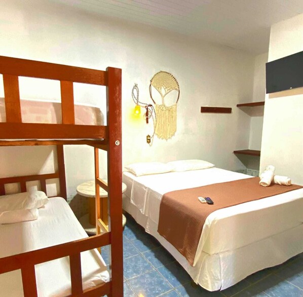 Una habitación pequeña y funcional con literas, una cama individual, un taburete pequeño y un estante en la pared.