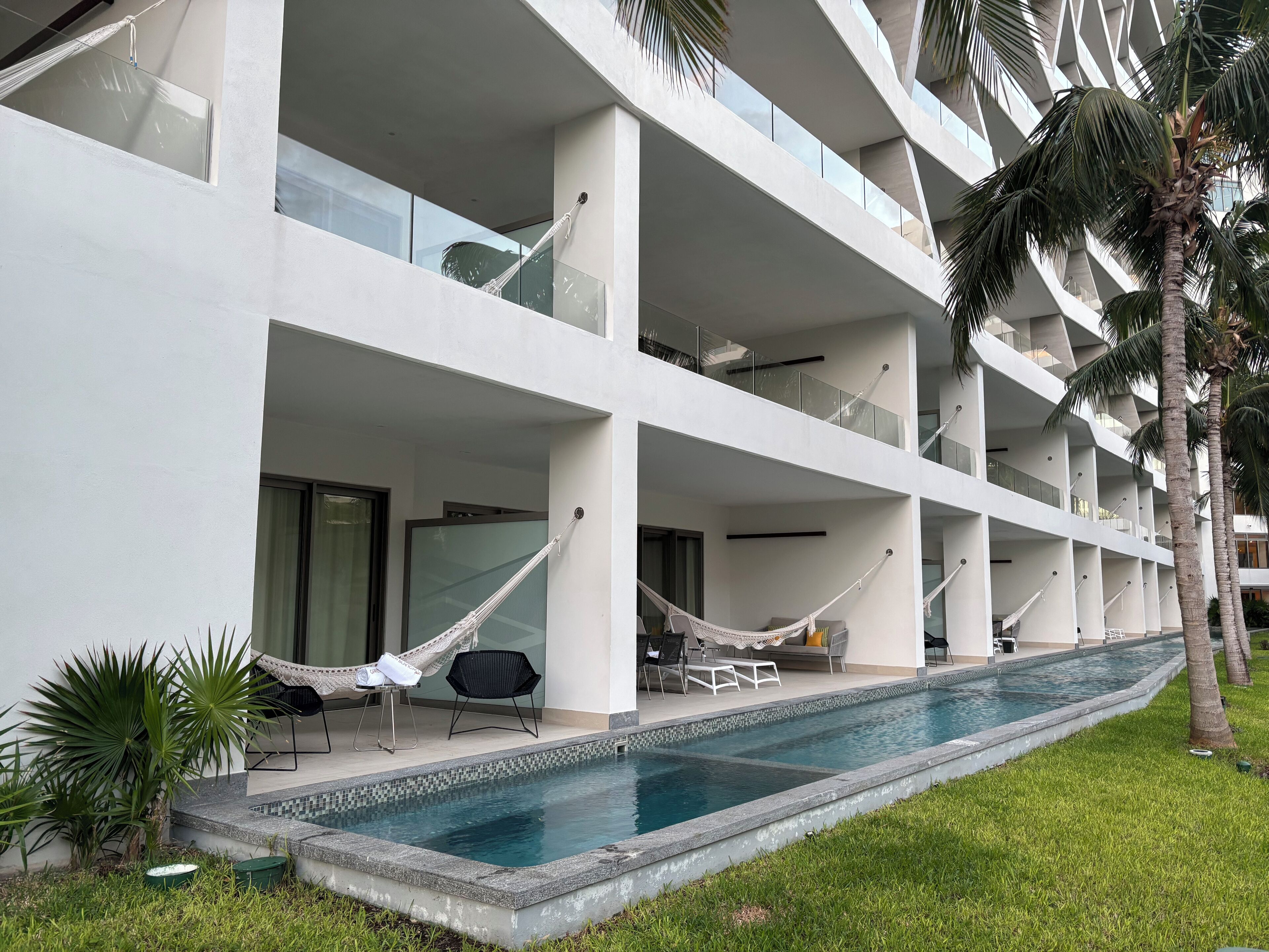Un hotel a più piani con piscina, area salotto esterna e palme.
