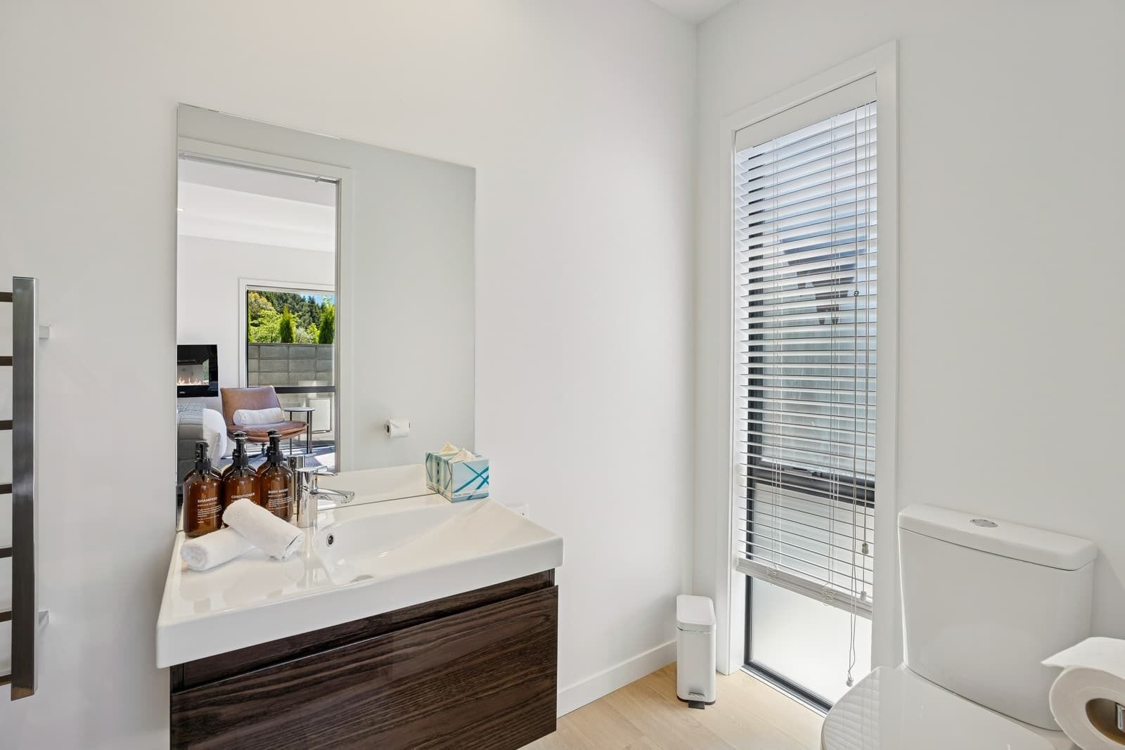A modern bathroom with a large mirror, a white sink, and a window with blinds.