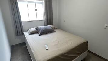 Una habitación pequeña y limpia con cama, aire acondicionado y ventana con cortinas.