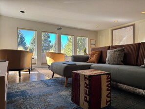 A modern living room with a sofa, armchair, and ottoman, large windows, and a decorative box. - Welcome to your perfect in-town Bend Winter Getaway! 30+ Day Minimum Rental! (Bend)