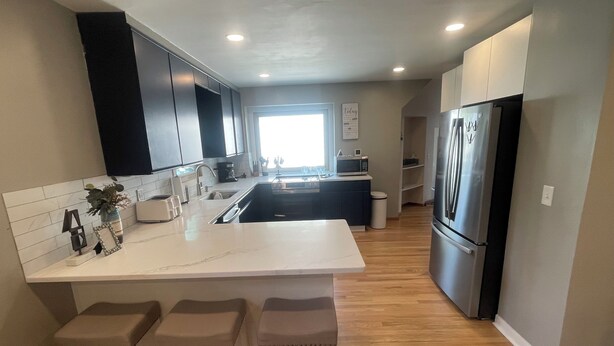 A modern kitchen with a central island, bar stools, a refrigerator, and a microwave. - Comfort & Space: 5BR Family Getaway w/ Pool, Fire Table, and game room! (Omaha)