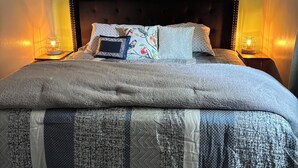 A bedroom with a large bed, a ceiling fan, a wall-mounted abstract painting, and two bedside lamps. - Comfort & Space: 5BR Family Getaway w/ Pool, Fire Table, and game room! (Omaha)