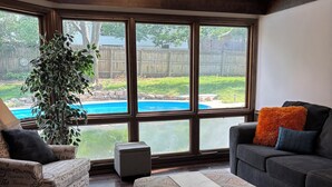 A living room with a large window, a pool, and a modern ceiling light fixture. - Comfort & Space: 5BR Family Getaway w/ Pool, Fire Table, and game room! (Omaha)