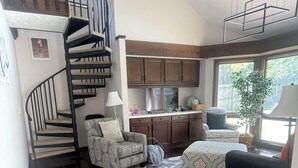 A spacious living area with a wooden floor, a spiral staircase, a kitchen with wooden cabinets, and a large window providing natural light. - Comfort & Space: 5BR Family Getaway w/ Pool, Fire Table, and game room! (Omaha)