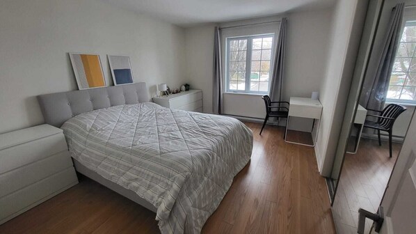 Een slaapkamer met een bed, nachtkastje, stoel en een raam met gordijnen.