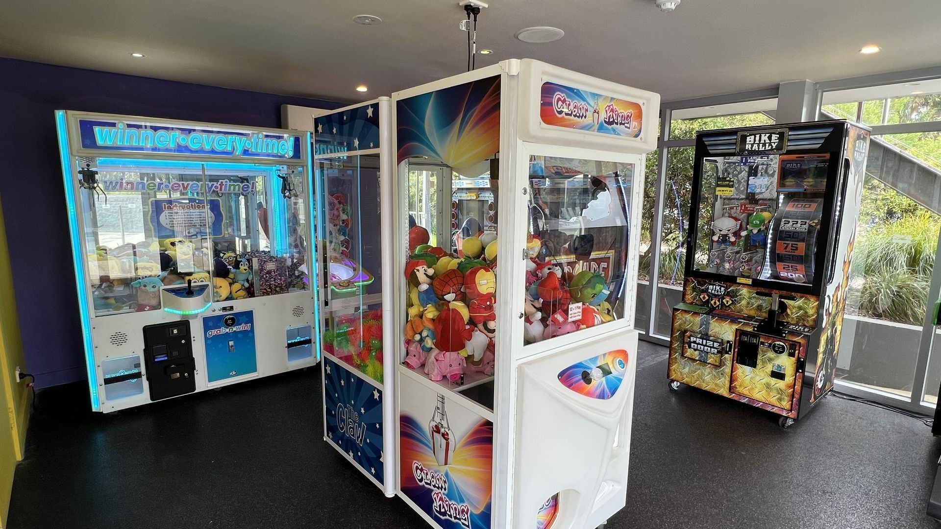 A row of claw machines in a brightly lit indoor area with large windows.