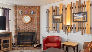 Ein Wohnzimmer mit Kamin aus Ziegelsteinen, einem roten Ledersessel, einem Holztisch und einem Fernseher.