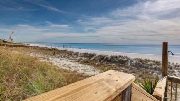 Eine Holzterrasse mit Blick auf einen Strand, mit Holzzaun und einem Holzpfosten.
