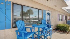 Ein Gebäude mit einer überdachten Terrasse, auf der blaue Stühle und ein kleiner Tisch stehen.