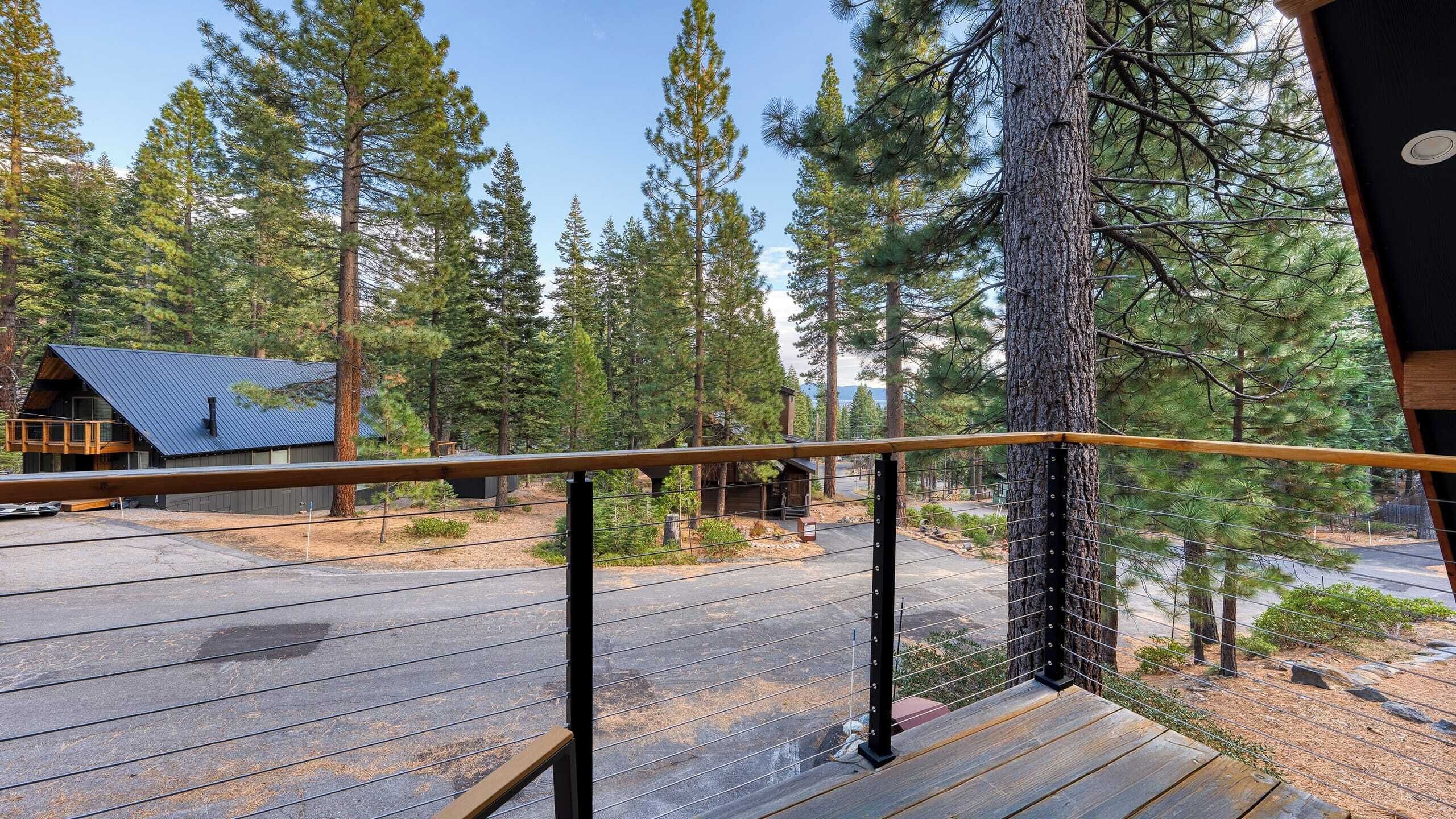 Une terrasse en bois, dotée d’une rambarde métallique, qui offre une vue sur une zone boisée où s’élèvent de grands pins.