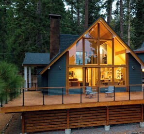 A cabin with a glass facade, wooden deck, and a staircase leading to the entrance. - Retreat With Lake Access, Deck & Modern Interior Agate Peak by Avantstay (Carnelian Bay)
