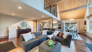 A spacious living area with a large sofa, a dining table, and a kitchen in the background. - Retreat With Lake Access, Deck & Modern Interior Agate Peak by Avantstay (Carnelian Bay)
