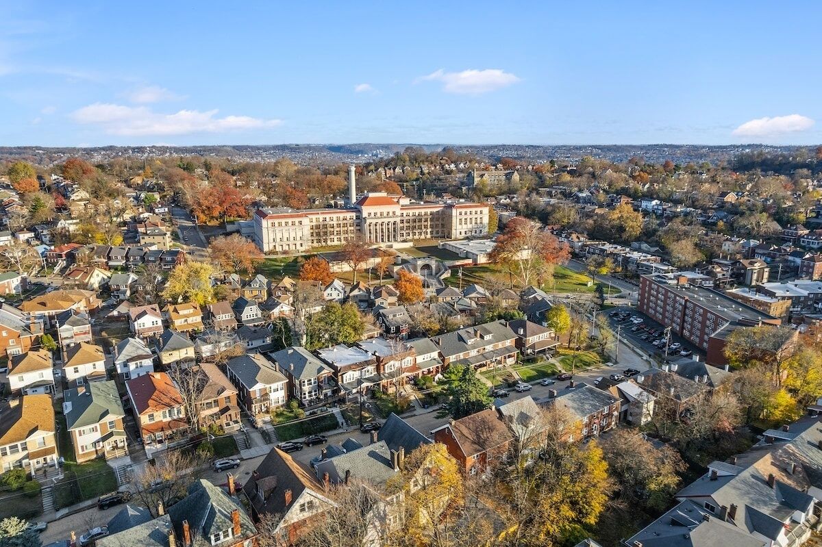 Un quartier résidentiel où se trouve un bâtiment imposant qui semble être une école ou une université, entouré de maisons et d’arbres.