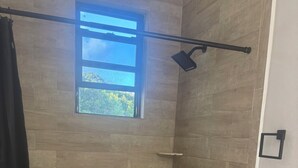 Een badkamer met een douche, een raam, een toilet en een betegelde vloer.