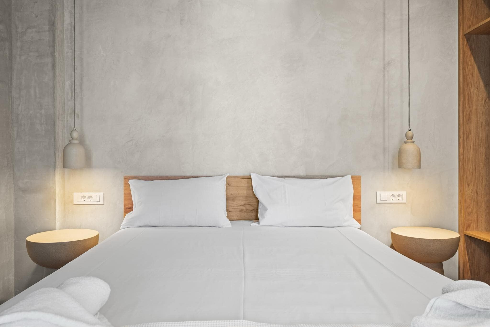 Une chambre à coucher moderne avec un grand lit, une tête de lit en bois, des tables de chevet avec des lampes et une palette de couleurs neutres.