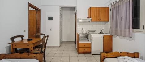 A compact room with two wooden beds, a small kitchenette, a dining table with chairs, and a bathroom door.