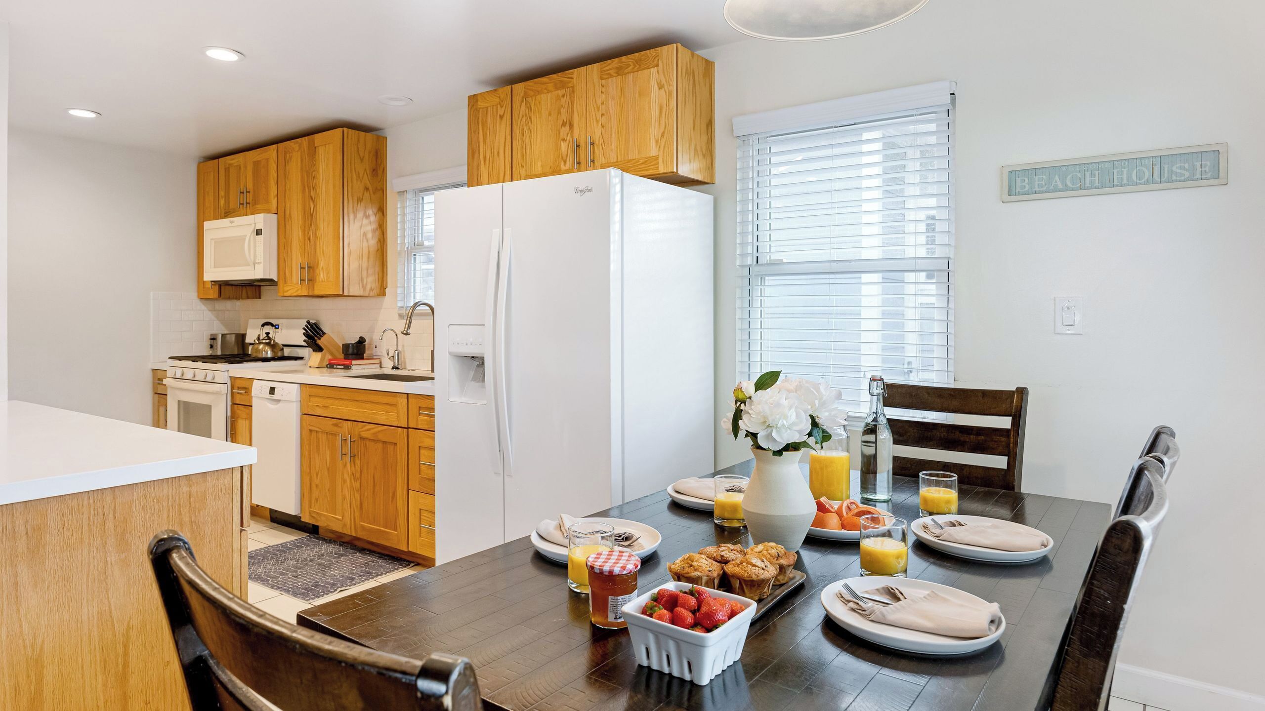 A modern kitchen with wooden cabinets, a white refrigerator, and a dining area with a table set for breakfast.