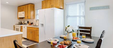 A modern kitchen with wooden cabinets, a white refrigerator, and a dining area with a table set for breakfast.