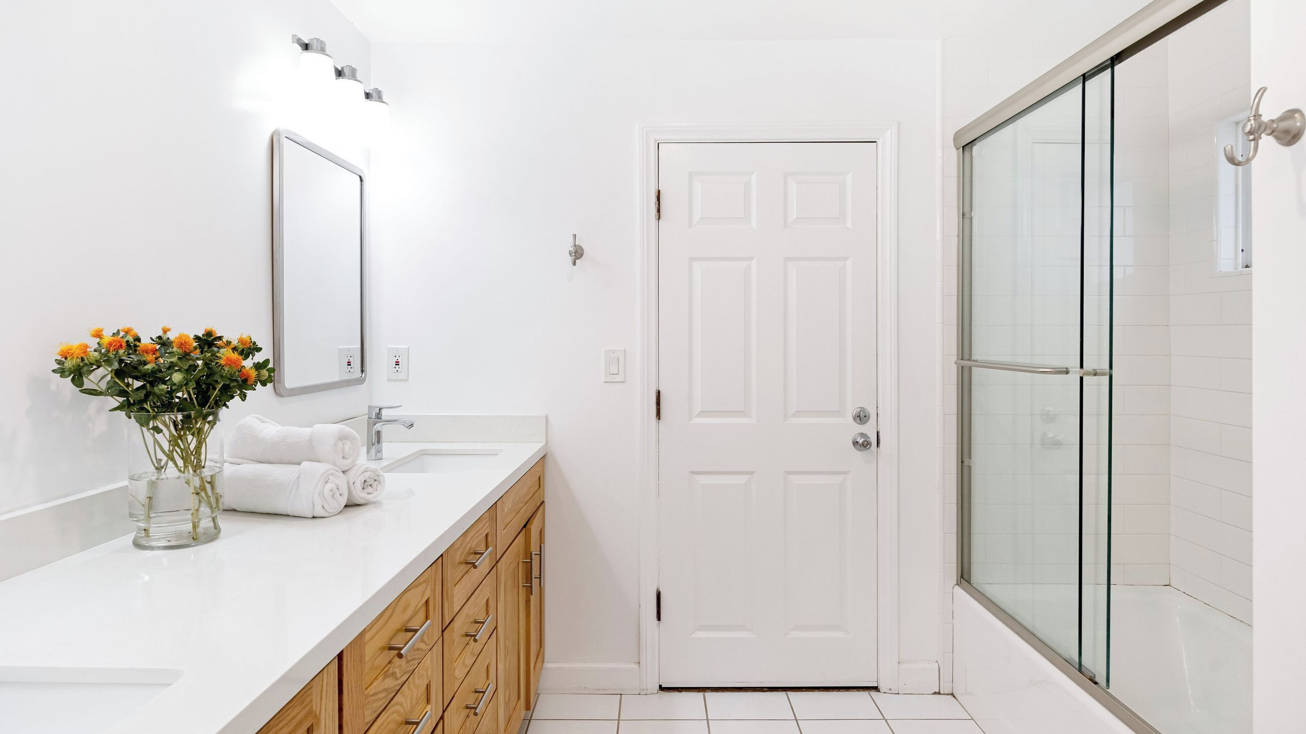 A bathroom with a white vanity, a glass shower enclosure, and a white door.