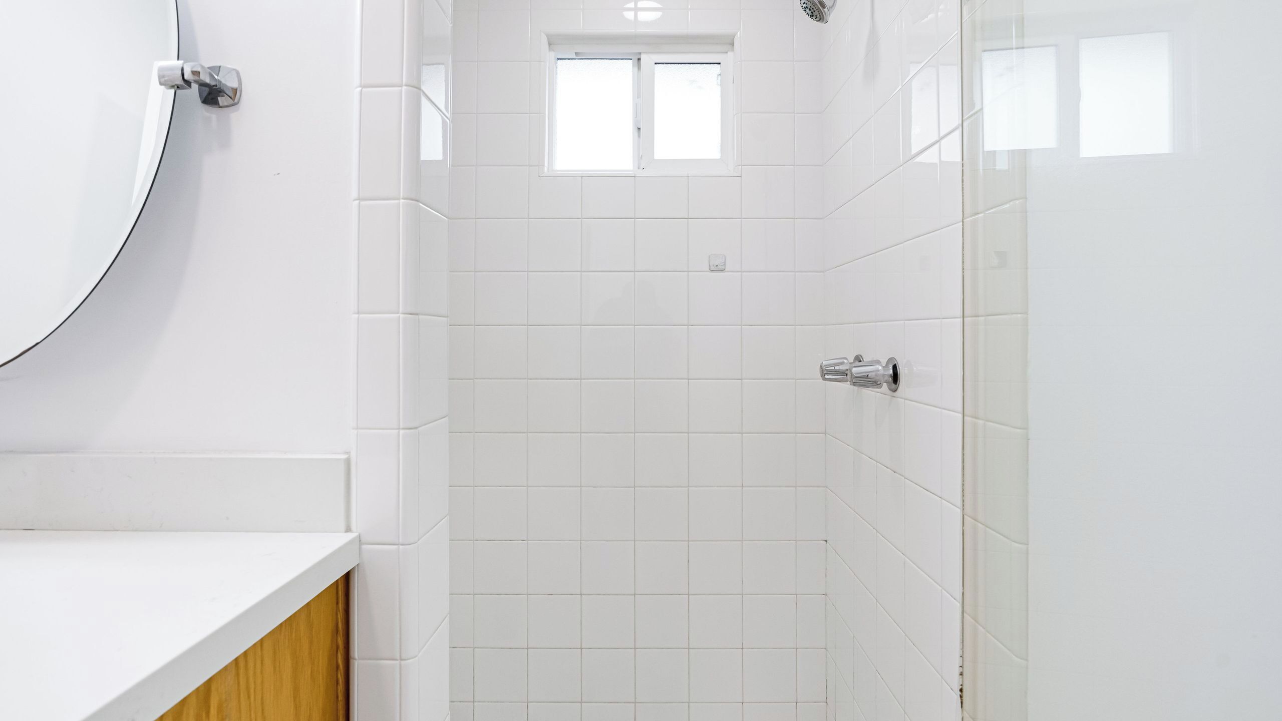 A bathroom with white tiles, a shower, and a window.