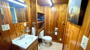 Un bagno con rivestimenti in legno, un lavabo, un water e scaffali.