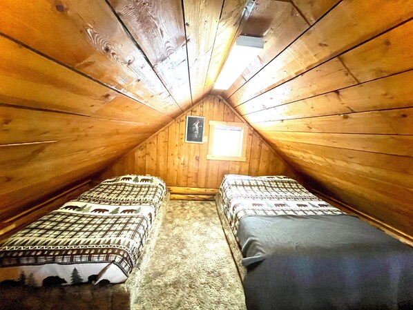 Une chambre mansardée chaleureuse, avec deux lits, une fenêtre et un tableau encadré au mur.